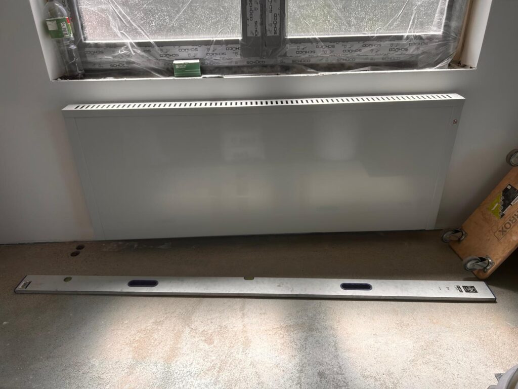 Nachtspeicher und Flächenspeicherheizung – der Unterschied in vier Punkten Weiße Flächenspeicherheizung, 162 cm breit und 8 cm tief, unter einem Fenster an der Wand montiert, davor eine 2-Meter-Wasserwaage als Größenvergleich